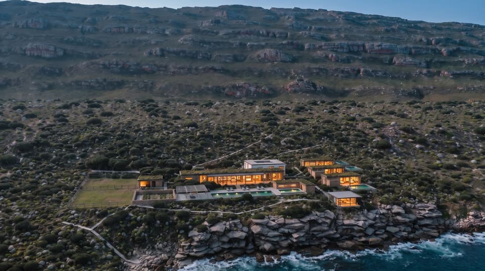 The estate from above the sea at dusk, every window lit, the pools glowing, the sandstone slope dark behind