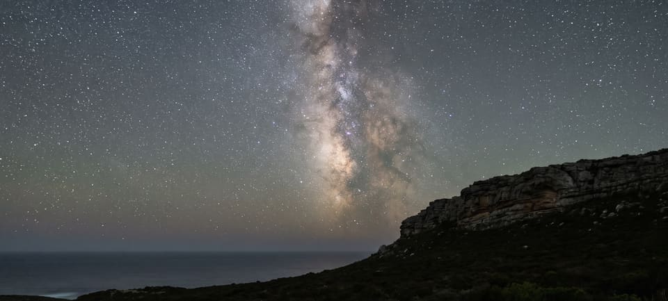 The Milky Way rising over the sea beside the dark sandstone ridge on a moonless night